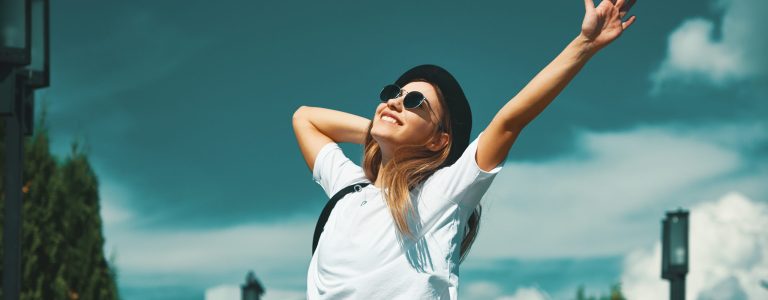 Freedom young woman carefree and happy with open arms on blue sky with hypnotizing sky in background. Caucasian girl in white shirt and jeans, feeling happiness enjoying her travel vacation